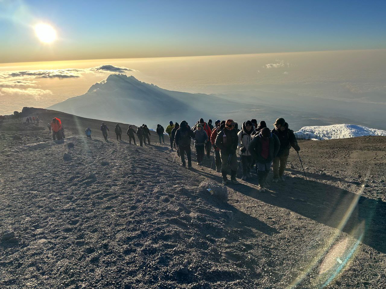 Kilimanjaro summit sign at Uhuru Peak with climbers, sunrise light